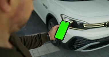 A man holding a green smartphone next to a white car video