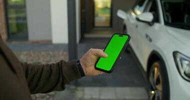 Man holding smartphone with green screen in front of car video