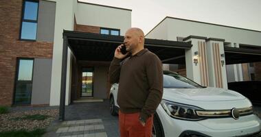 A bald man talking on a cell phone in front of a house video