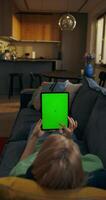 ein Frau ist Sitzung auf ein Couch mit ein Tablette Computer mit ein Grün Bildschirm video