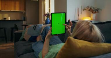 A woman is using a tablet with a green screen on the couch video