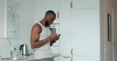 A man in a white tank top is looking at his phone video