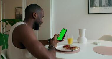A man sitting at a table with a green phone and a plate of food video