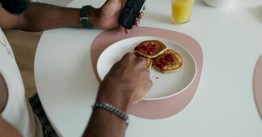 A man is eating pancakes on a plate with a cell phone video
