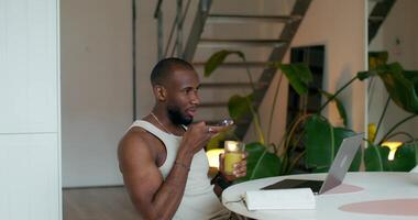 A man in a tank top is sitting at a table with a laptop video