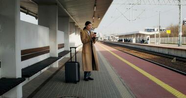 A woman in a coat standing on a platform with a suitcase video