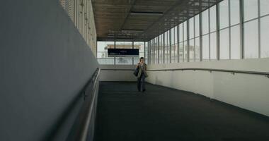 A man walking down an empty hallway with a large window video
