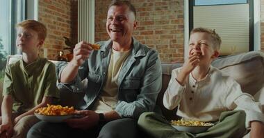 A man and two boys sitting on a couch eating popcorn video