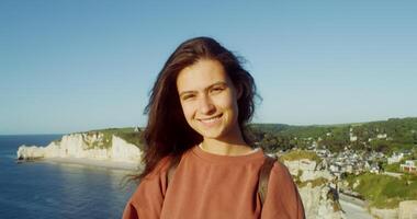 A young woman smiles while standing on a cliff overlooking the ocean video