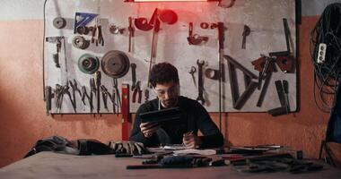 A man sitting at a table with tools and a laptop video