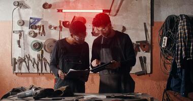 Two men in a workshop looking at a tablet video