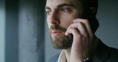 A man with a beard and suit talking on a cell phone video
