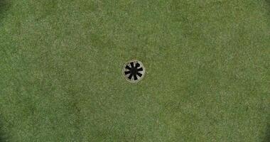 An overhead view of a golf course set on artificial turf. The golf ball rolls up to the hole and spins around its circumference video