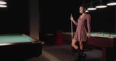 A woman in a dress standing next to a pool table video
