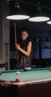 A woman in a leather vest is standing next to a pool table video