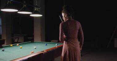 A woman in a dress is standing next to a pool table video