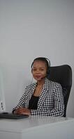 A woman wearing a headset sitting at a desk with a computer video