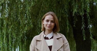 A woman in a trench coat standing in front of a tree video