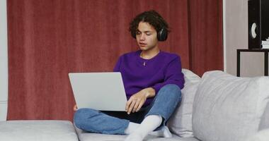 A woman sitting on a couch with headphones using a laptop video