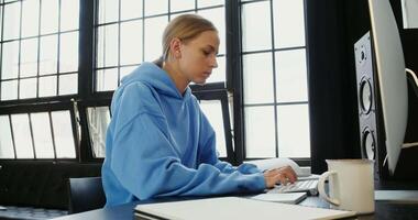 A woman in a blue sweatshirt is sitting at a desk with a laptop video