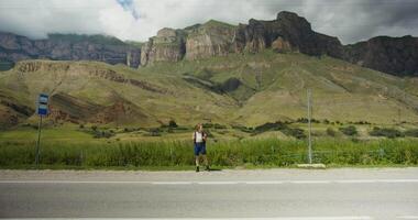 A man standing on the side of the road in front of a mountain video