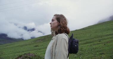 A woman standing in the middle of a field with a backpack video