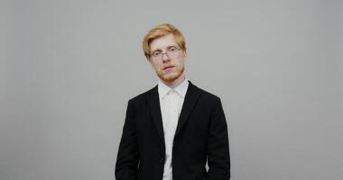 A man in a suit and glasses standing in front of a gray background video