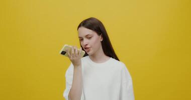 A woman holding a cell phone in front of a yellow background video