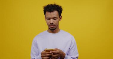 A man is looking at his phone while standing against a yellow background video