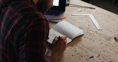 A man is working on a notebook with a laptop video