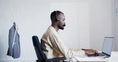 A man wearing a headset and sitting at a desk with a laptop video