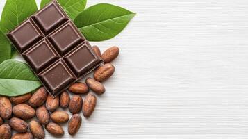 Chocolate and cocoa beans on white wooden table with green leaves photo