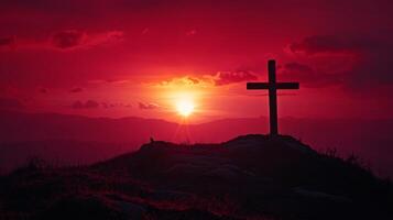 Christian cross stands on hill. Sunset colors the sky red. Simple faith image. Hope and religion. Cross silhouette on landscape. Sun shines brightly. photo