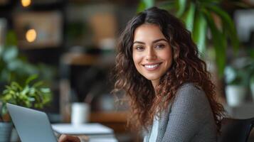 Woman with laptop sits smiling in bright office. Plants in background. Business meeting or student study environment with natural light. photo