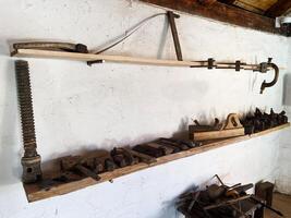 Rustic workshop tools displayed on wooden shelves against a white plastered wall photo