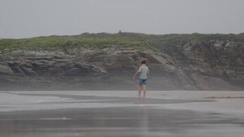 Teen walking alone on a misty beach, surrounded by cliffs and enjoying the serene atmosphere of nature video
