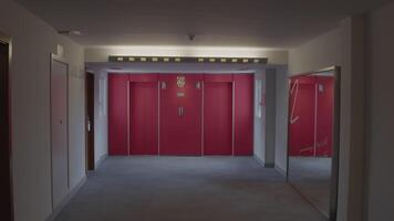 Camera moves forward through an empty hotel corridor, revealing two red elevators and a mirror at the far end video