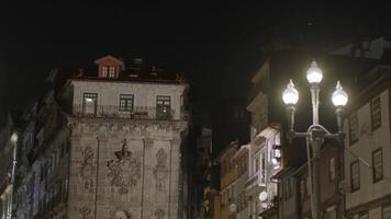 A historical stone building with intricate carvings and a red rooftop window illuminated at night in Porto, Portugal, surrounded by traditional architecture and a glowing streetlamp video