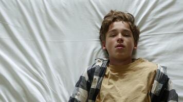 Teenager lying on a white bed sheet, displaying a thoughtful expression while contemplating various concerns and issues video