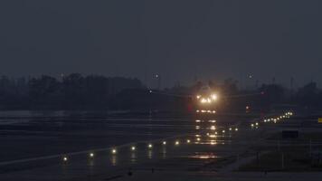 Passenger airplane landing on a runway at night with lights reflecting on wet surface video