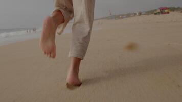 Close up of barefoot steps on a sunlit beach. Capturing the carefree movement and soft sand textures, with waves in the background inviting relaxation, filmed in slow motion video
