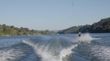 Senior sportswoman waterskiing on a serene lake, showcasing skill and speed under a bright blue sky on a sunny summer day video