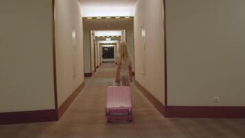 Little girl around 7 years old walking down a hotel hallway pulling a pink polka dot suitcase, filmed from the back with no face visible. video