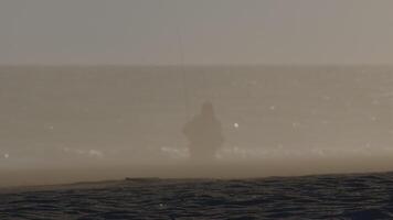 Silhouette of fisherman casting fishing rod in misty ocean surf, creating a serene and evocative scene of solitude and connection with nature video