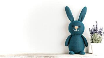 A handcrafted teal rabbit toy is placed on a light wooden surface, accompanied by a small pot of lavender flowers. The setting is cozy and inviting. photo
