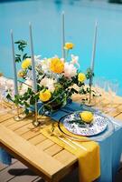 Plate with a yellow lemon and an olive branch stands on a festive table near a bouquet of flowers photo