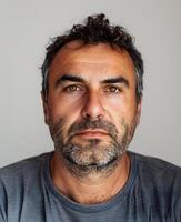 Man in gray shirt with beard, looking at camera with visible collar and sleeves photo