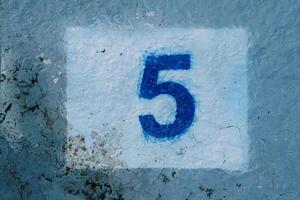 Number five painted on a blue mud-stained wall in a white rectangle photo