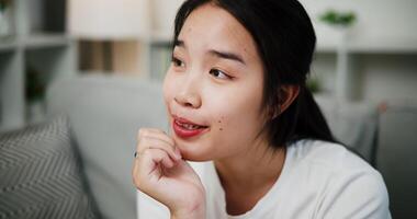 Handheld selective focus shot, Young Asian woman sits on a sofa relaxed and smiles happily after hearing something that makes her feel good or relieved. video