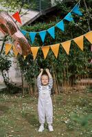 Little smiling girl stands under colorful flags holding an inflatable number 3 by a string photo